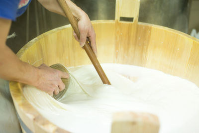 High angle view of worker mixing mozzarella cheese with ladle in wooden container at factory