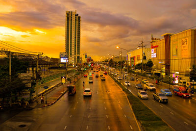 Cars on city street against sky during sunset