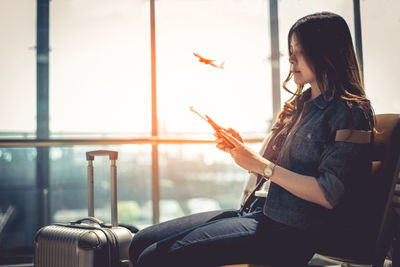 Woman using smart phone while sitting at departure area in airport