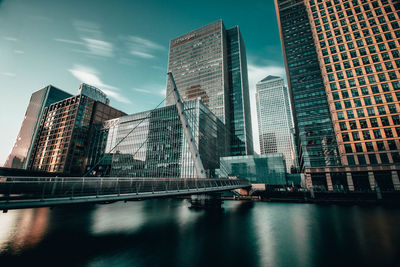 Modern buildings by river against sky in city