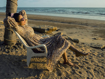 Woman relaxing on sand at beach against sky