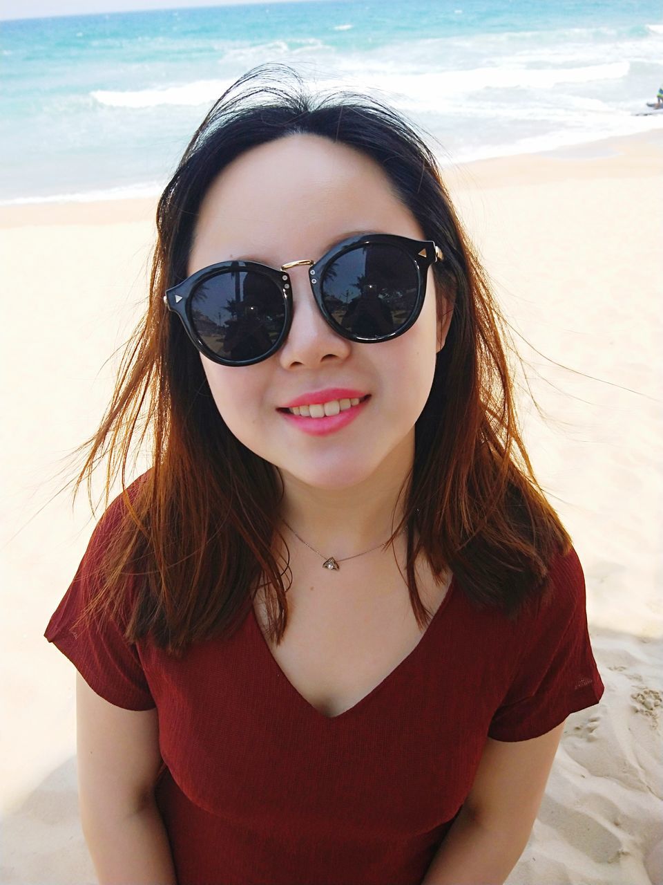 sunglasses, beach, sea, sand, looking at camera, real people, front view, portrait, one person, long hair, young women, leisure activity, outdoors, beautiful woman, young adult, vacations, day, nature, smiling, lifestyles, horizon over water, close-up, sky, water, beauty in nature