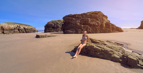 Full length of woman sitting on rock at beach against sky