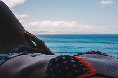 Low section of woman relaxing by sea against sky