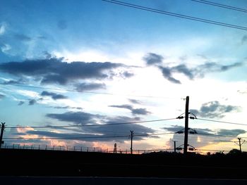 Silhouette of electricity pylons against cloudy sky