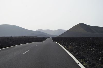 Scenic view of road by mountains against clear sky