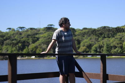 Young man looking at view while standing on footbridge against lake