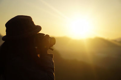 Rear view of woman photographing against sky during sunrise