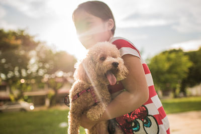 Smiling girl carrying poodle puppy while standing on field