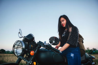 Portrait of young woman sitting on motorcycle against clear sky