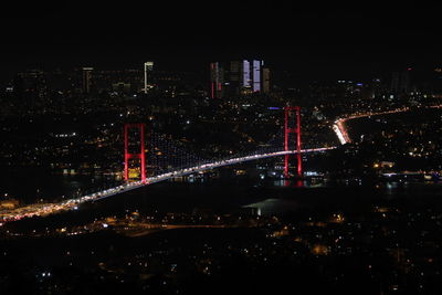 Illuminated bridge over river by buildings against sky at night