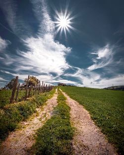 Dirt road amidst field against sky