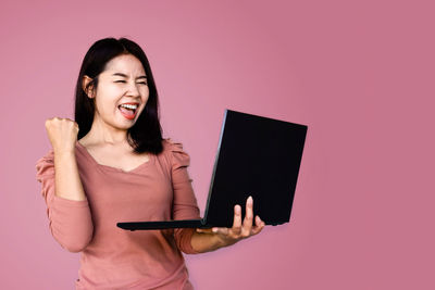 Smiling young woman using mobile phone against gray background