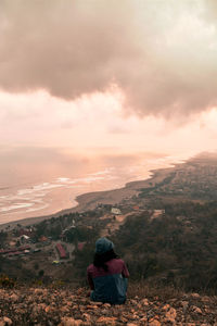 Rear view of woman looking at landscape against sky during sunset