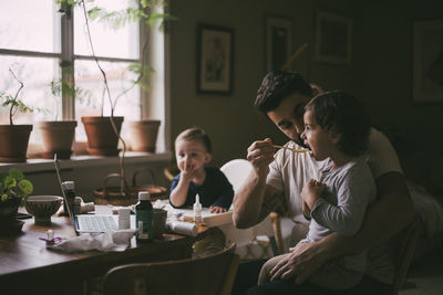 Father feeding son in living room at home