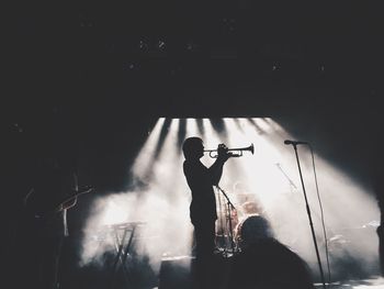 Silhouette man playing trumpet with performer in smoke