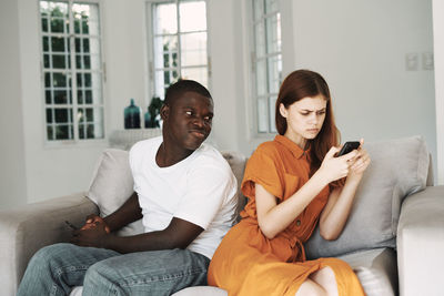 Sad man and woman using phone while sitting on sofa