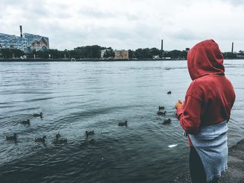 Rear view of man standing by river against sky