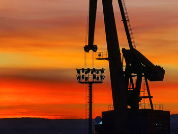 Silhouette cranes at construction site during sunset