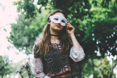 Portrait of young woman standing against tree