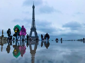 Reflection of people on water against cloudy sky