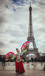 Woman in traditional clothing with hand fan standing against eiffel tower