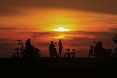 Silhouette people against orange sky during sunset