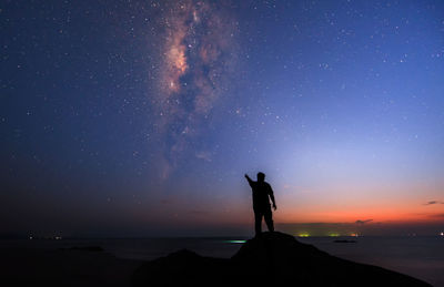 Silhouette man standing while pointing at galaxy in sky