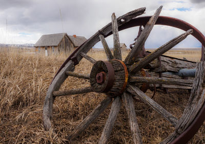 Close-up of abandoned wheel on grassy field against cloudy sky