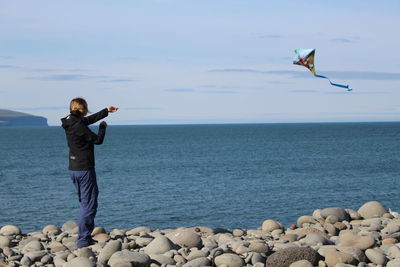 Full length 0f woman flying kite while standing at beach against sky