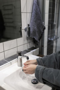 Cropped hands of woman washing under faucet in bathroom sink