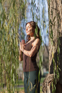 Young woman standing by tree trunk