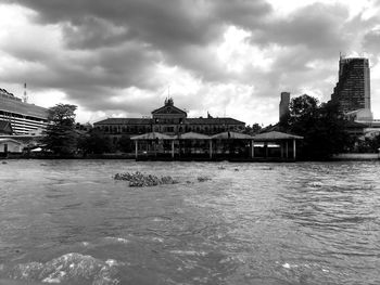 View of buildings by river against cloudy sky