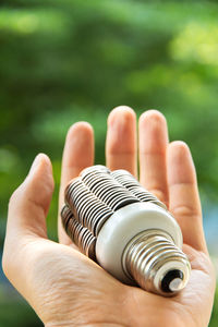 Cropped hand of man holding light bulb against plants