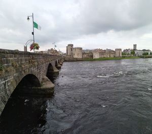 Bridge over river by buildings against sky