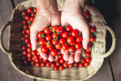 Cropped hands holding cherry tomatoes over wicker basket