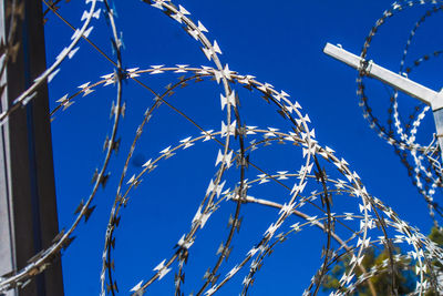 Low angle view of razor wire fence against clear blue sky