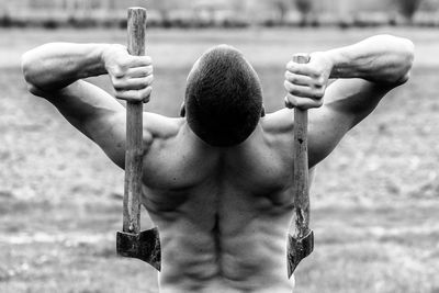 Rear view of a shirtless man holding axes
