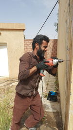 Side view of man drilling wall with power drill