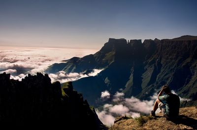 Rear view of hiker sitting on mountain against sky