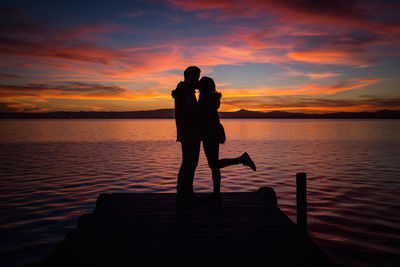 Silhouette people standing on shore against orange sky