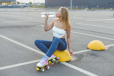 Young woman drinking water while sitting on road