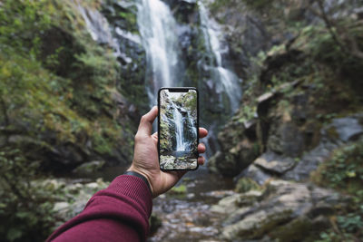 Midsection of person photographing with mobile phone on rock