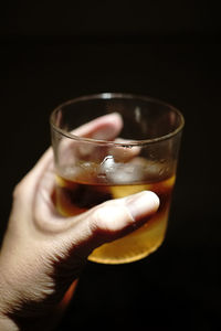 Close-up of hand holding wineglass against black background