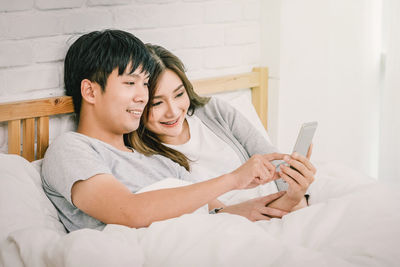 Young woman using mobile phone while sitting on bed at home