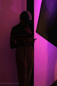 Side view of woman standing against pink wall at home