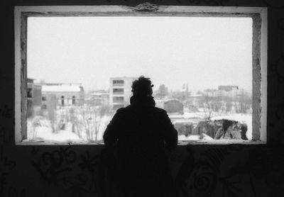 Rear view of silhouette man looking through window