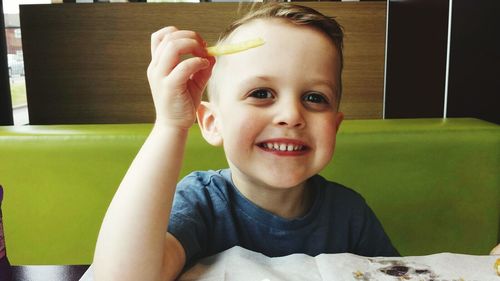 Close-up portrait of happy boy holding french fries while sitting at restaurant