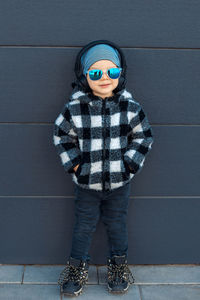 Portrait of cute boy wearing sunglasses standing against wall outdoors