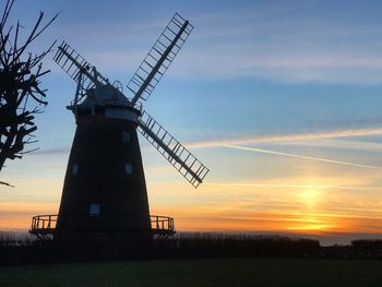 Silhouette of traditional windmill on field against sky during sunset